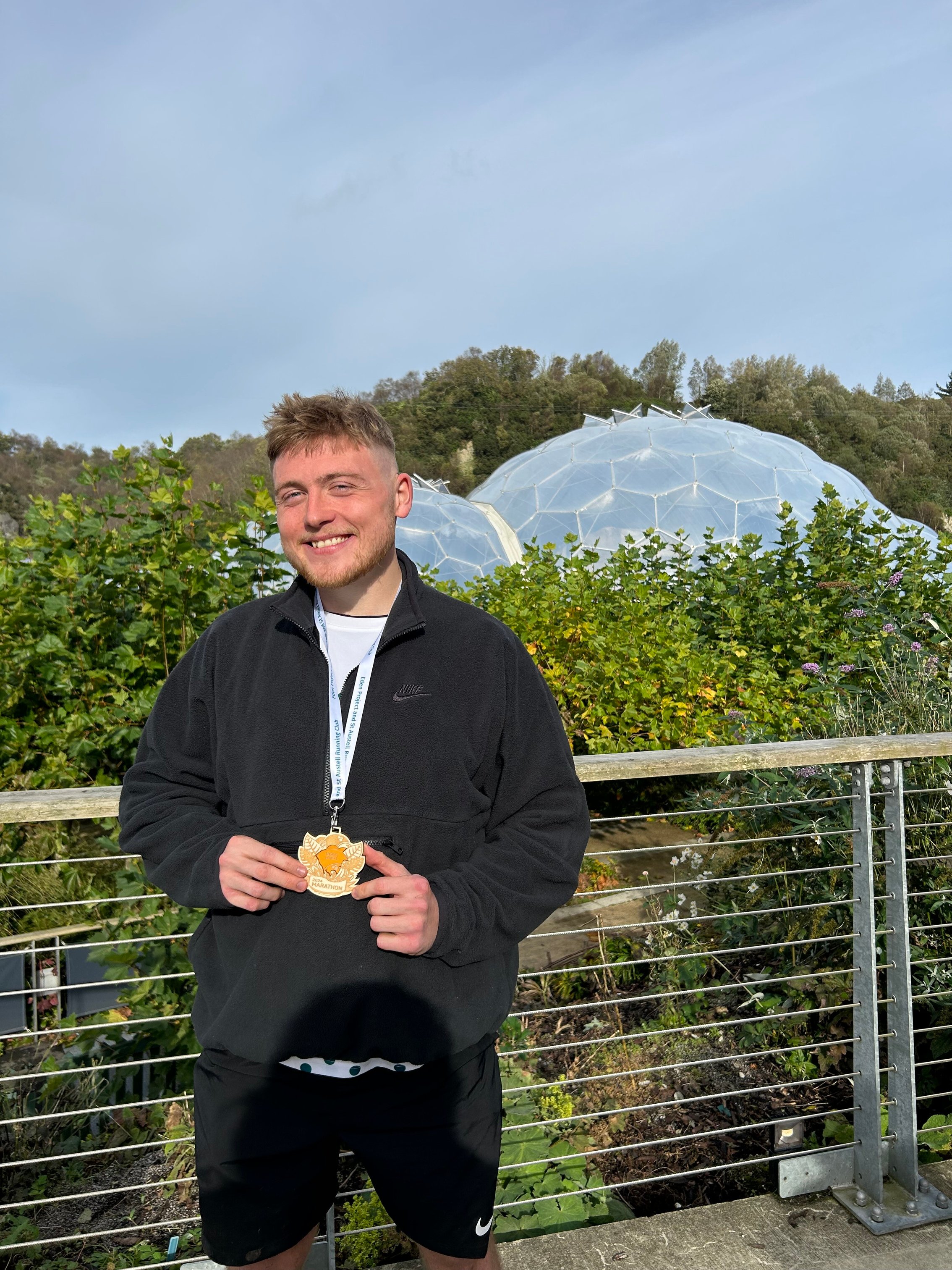 A photo of me posing with my medal in front of the iconic Eden Project domes. 