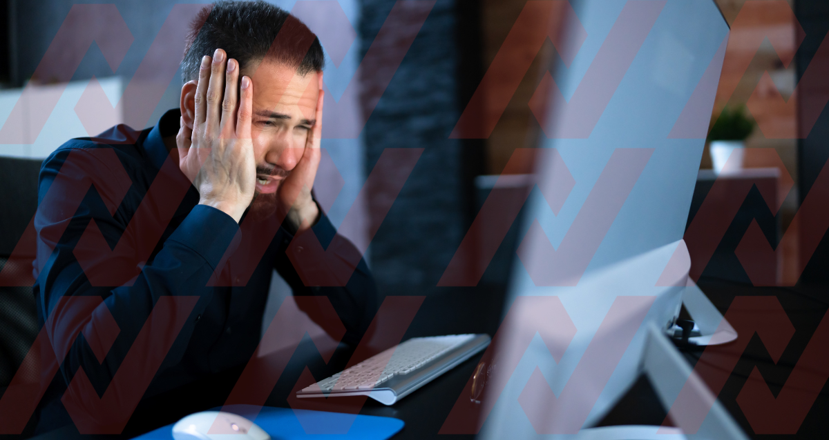 Photo of man looking at computer whilst looking distressed with his head in his hands. 