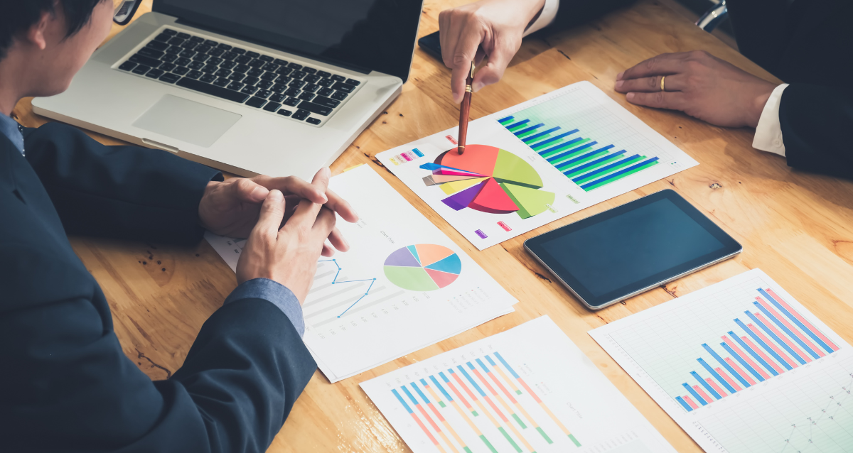 Photo of two people sat across from each other at a table. One person is pointing at a pie chart which may indicate financial planning. 