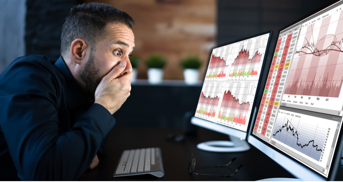 Photo of a man looking shocked whilst looking at various graphs on dual monitors.